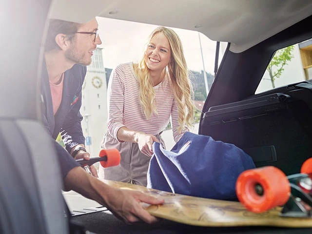 Two people are loading a vehicle with a skateboard and a bag.