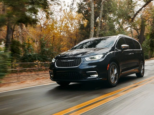 A Chrysler Pacifica van driving on a wet road in a forested area